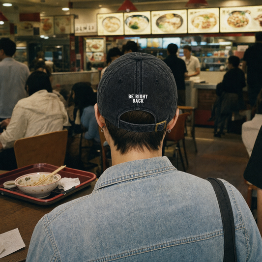 Be Right Back vintage cap in black, embroidery on the back, worn walking through a food hall
