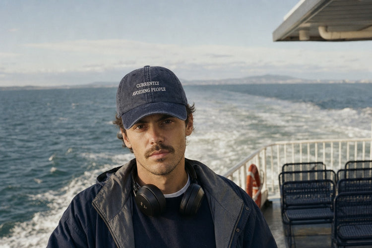 Currently Avoiding People embroidered vintage cap in navy, worn on a ferry deck