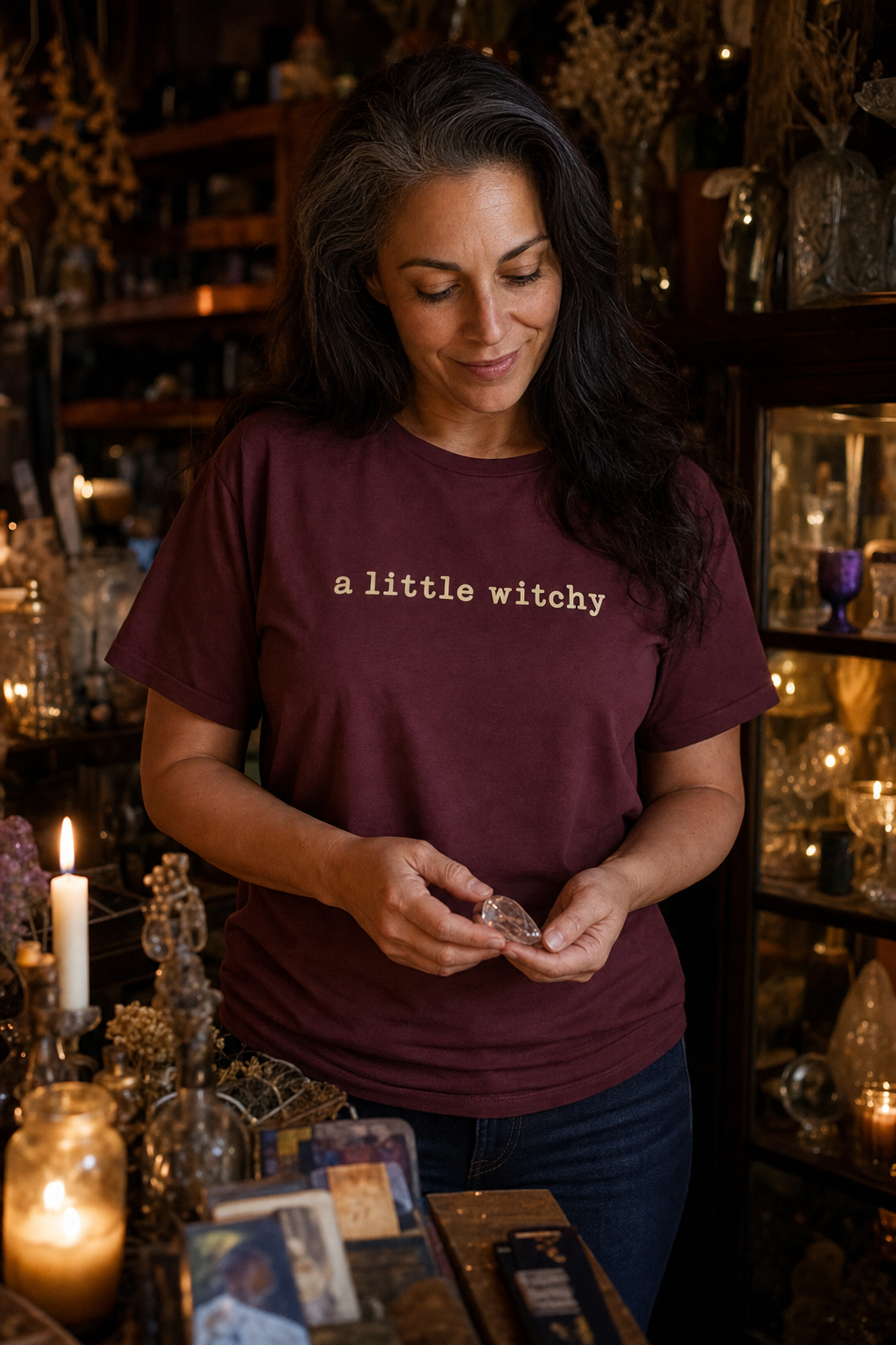Woman browsing a candlelit vintage shop wearing the maroon A Little Witchy tee