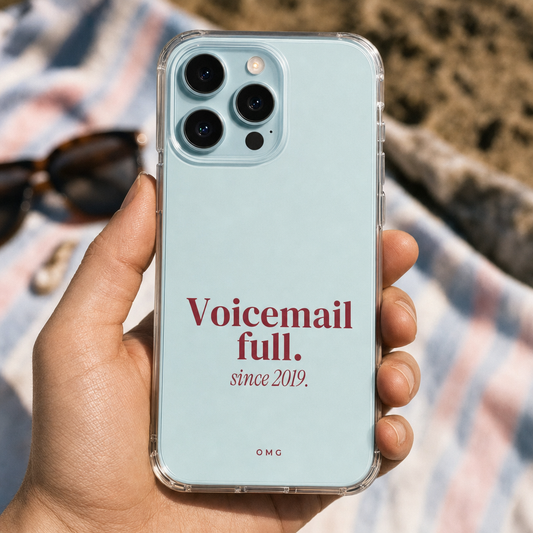 Clear iPhone case printed “Voicemail full. since 2019.” in dark rose, held over a beach towel
